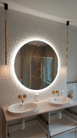 Nowoczesna łazienka z dwoma umywalkami, okrągłym lustrem podświetlanym LED, złotą armaturą i trójwymiarową białą tapetą.