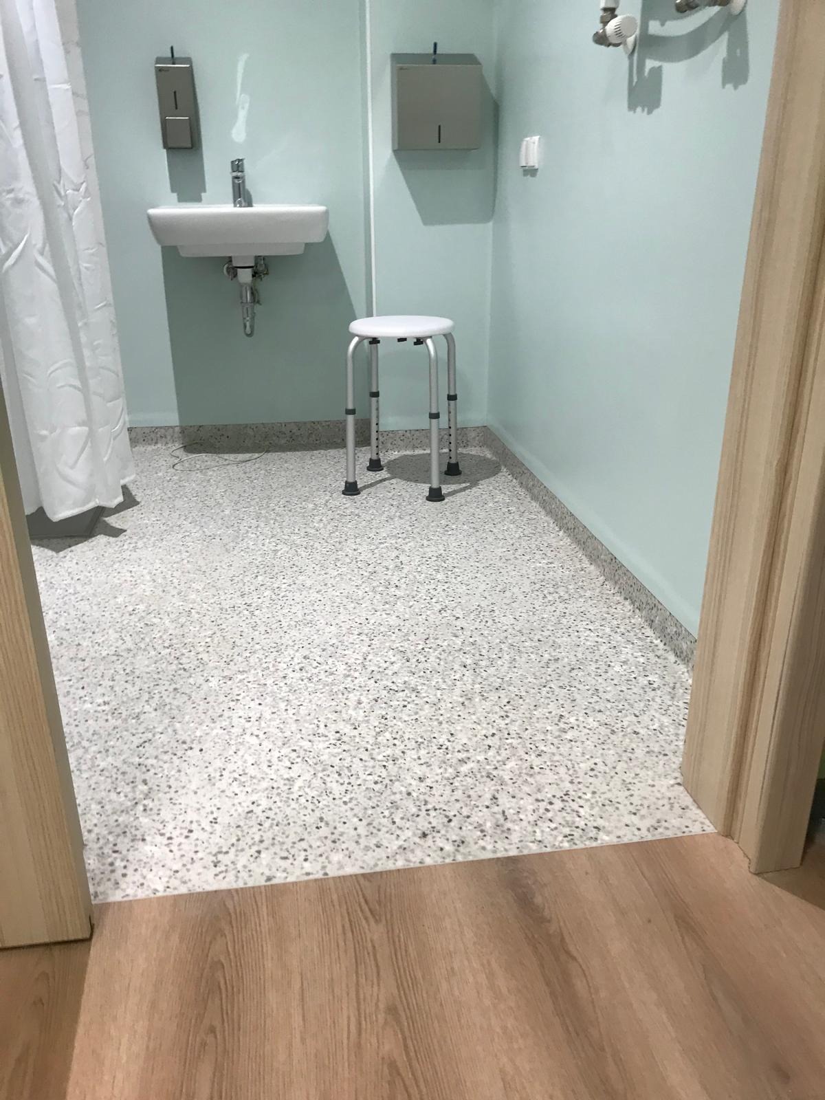 Wyremontowana łazienka w Bydgoszczy z umywalką, białym stołkiem i podłogą w szarym lastryko widziana zza drewnianej ościeżnicy.