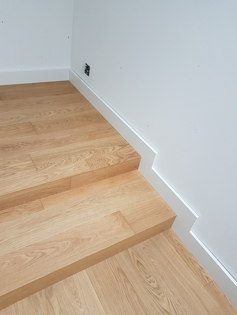 Jasny parkiet ułożony na schodach z białymi listwami przypodłogowymi dopasowanymi do stopni.
