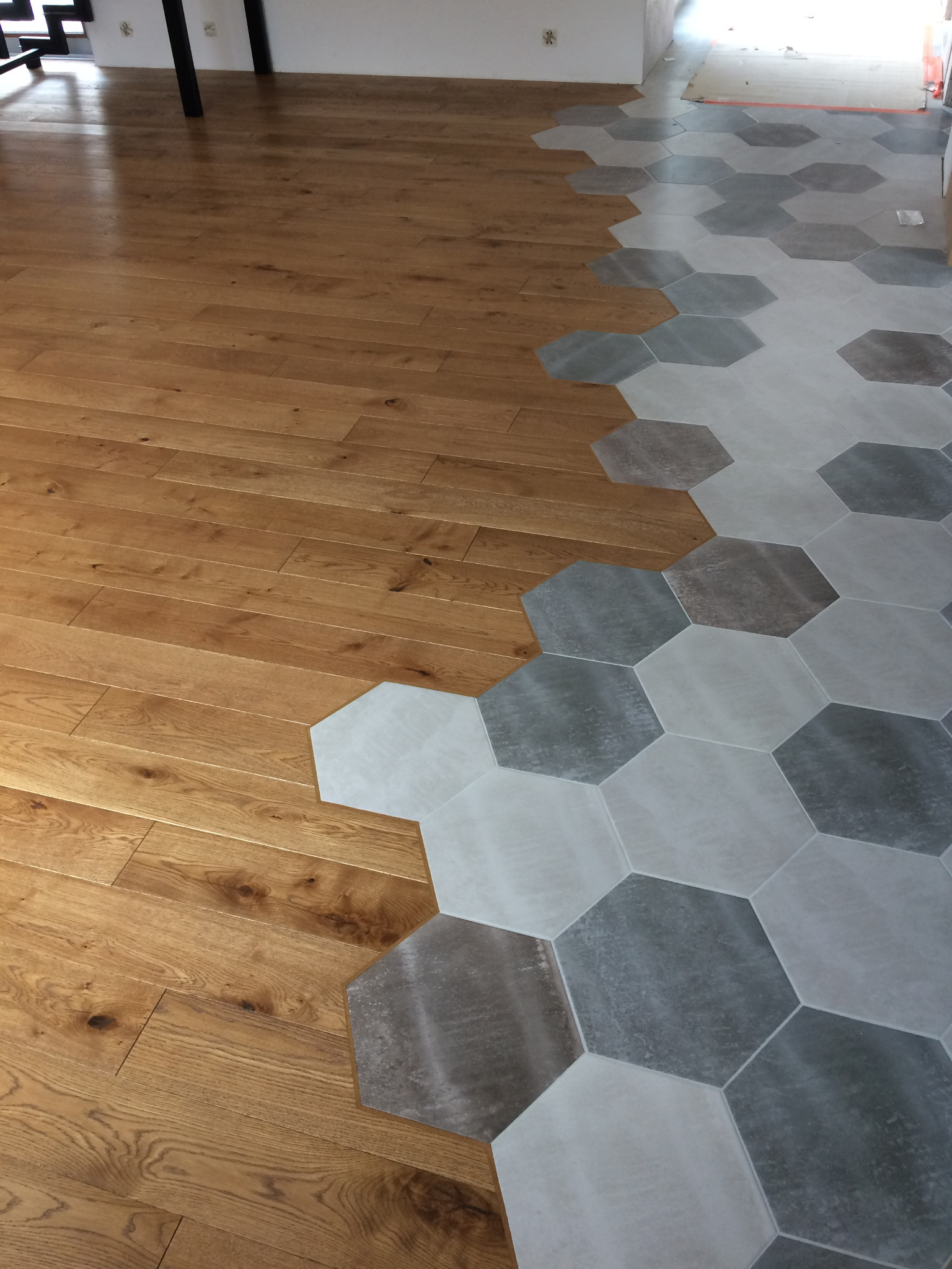 Połączenie parkietu z heksagonalnymi płytkami w odcieniach szarości i bieli, tworzące nowoczesny wzór na podłodze.