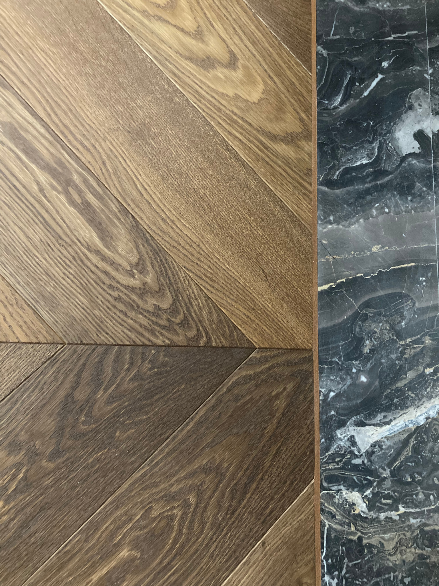 Parkiet ułożony we wzór jodełki francuskiej zestawiony z płytką imitującą czarny marmur.