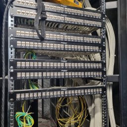 Eclipse Systems Poland - Patch panel w szafie rack z podłączonymi kablami Ethernet, żółty tester kabli na górze, widoczne kable ułożone w wiązki. Niektóre kable są podłączone, inne zwisają luźno.