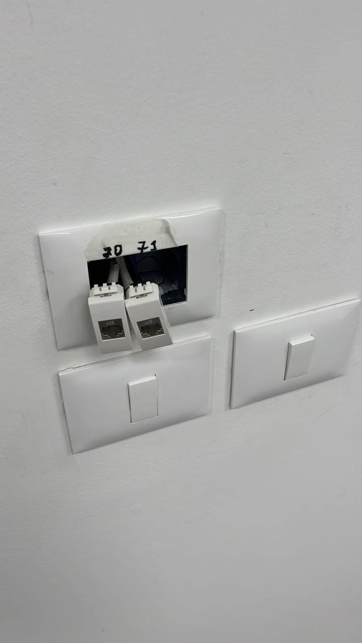 Uszkodzone gniazdo sieciowe z dwoma wpiętymi kablami Ethernet, widoczne ślady po taśmie i napisy '30 71' na obudowie, obok odłączone elementy ramki gniazda.