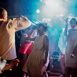 Piotr Klentak - Roztańczona grupa ludzi na parkiecie, dynamiczne ujęcie z podświetleniem, widoczna radość i energia.