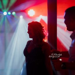 Piotr Klentak - Sylwetka kobiety w sukni wieczorowej pod światłami dyskotekowymi, z widocznym fotografem po prawej stronie kadru.