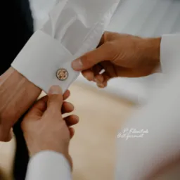 Mężczyzna zapinający mankiet białej koszuli z okrągłym, drewnianym spersonalizowanym spinką z wygrawerowanymi inicjałami i datą ślubu.