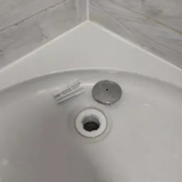 Umywalka narożna z elementami odpływu i drobnymi zabrudzeniami, obok leży związany gumką pakiet białych, plastikowych elementów montażowych.