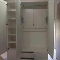 Wnętrze białej szafy z otwartymi drzwiami, widoczne półki po lewej stronie i drążki na ubrania oraz szuflady na dole, dwie szuflady są otwarte.