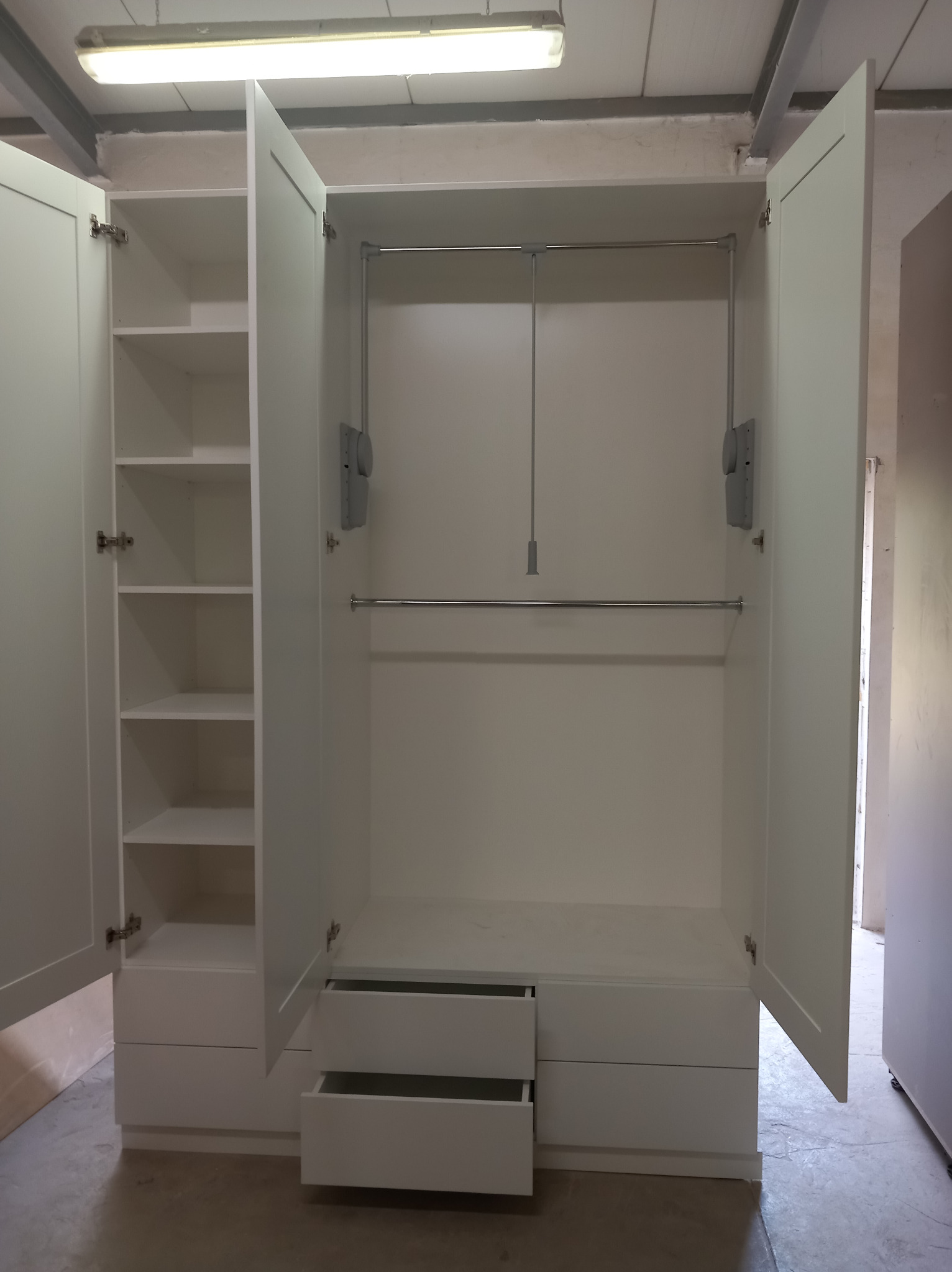 Wnętrze białej szafy z otwartymi drzwiami, widoczne półki po lewej stronie i drążki na ubrania oraz szuflady na dole, dwie szuflady są otwarte.