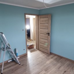 Wykończenia wnętrz - Pokój po malowaniu ścian na turkusowo, z drewnopodobną podłogą, otwartymi drzwiami i rozłożoną drabiną malarską.