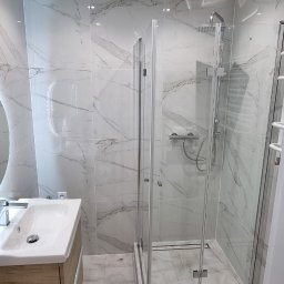 Wykończenia wnętrz - Nowoczesna łazienka z kabiną prysznicową typu walk-in, umywalką z szafką w odcieniach drewna i marmurowymi płytkami na ścianach i podłodze. Minimalistyczny design.