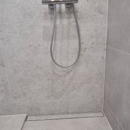 Wykończenia wnętrz - Nowoczesna kabina prysznicowa z odpływem liniowym i szarą, kamienną okładziną. Minimalistyczny design, chromowana armatura, precyzyjne ułożenie płytek.