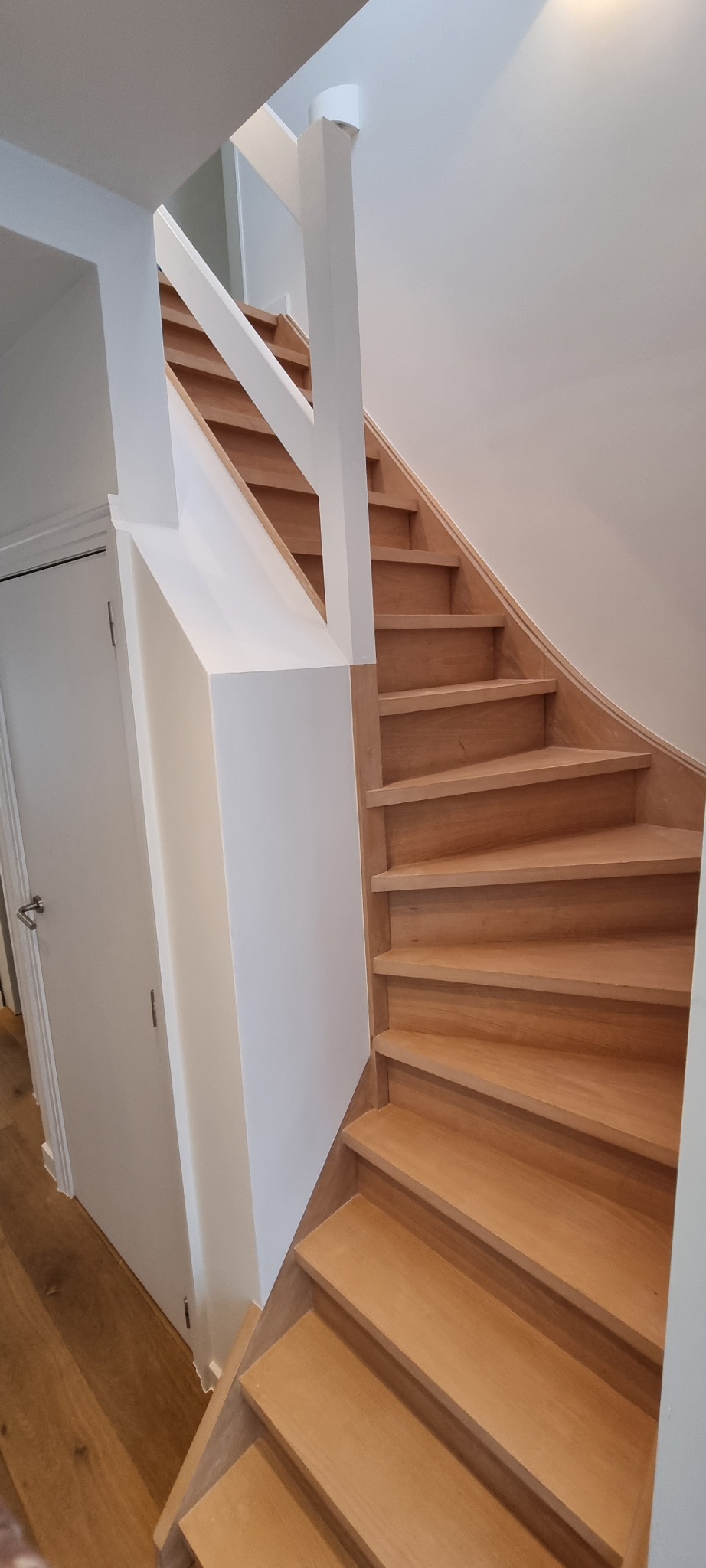 Jasne, drewniane schody z białymi ścianami i balustradą, widok z dołu, naturalne oświetlenie.