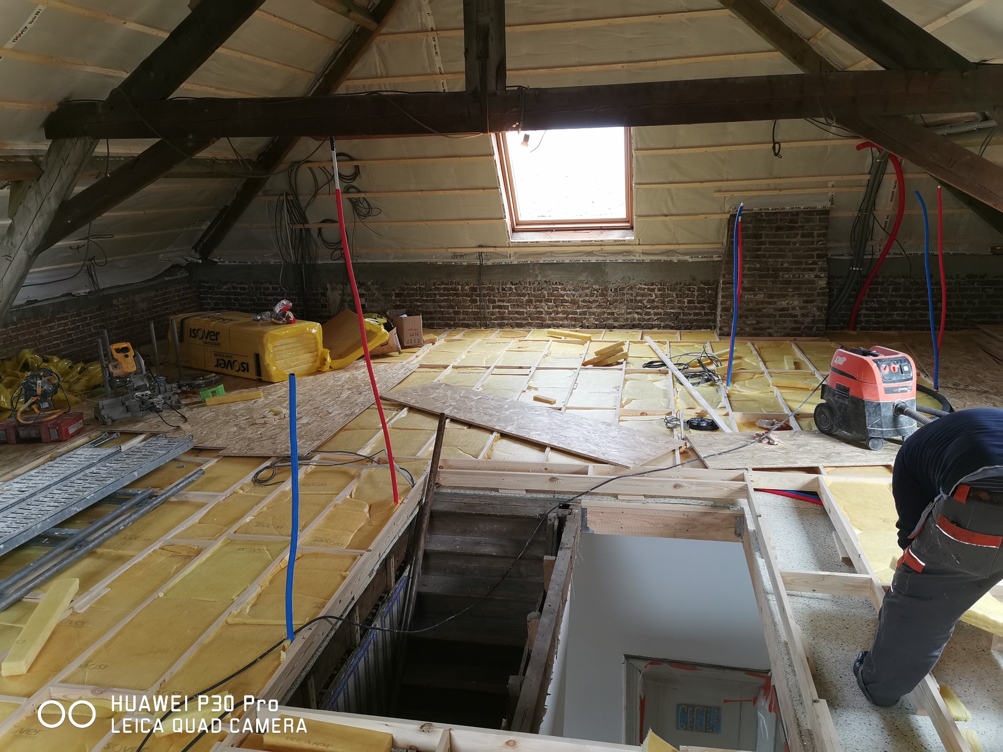 Poddasze w trakcie ocieplania: widoczne drewniane krokwie, okno dachowe, częściowo ułożona izolacja Isover pomiędzy legarami podłogowymi oraz instalacja elektryczna i hydrauliczna prowadzona...