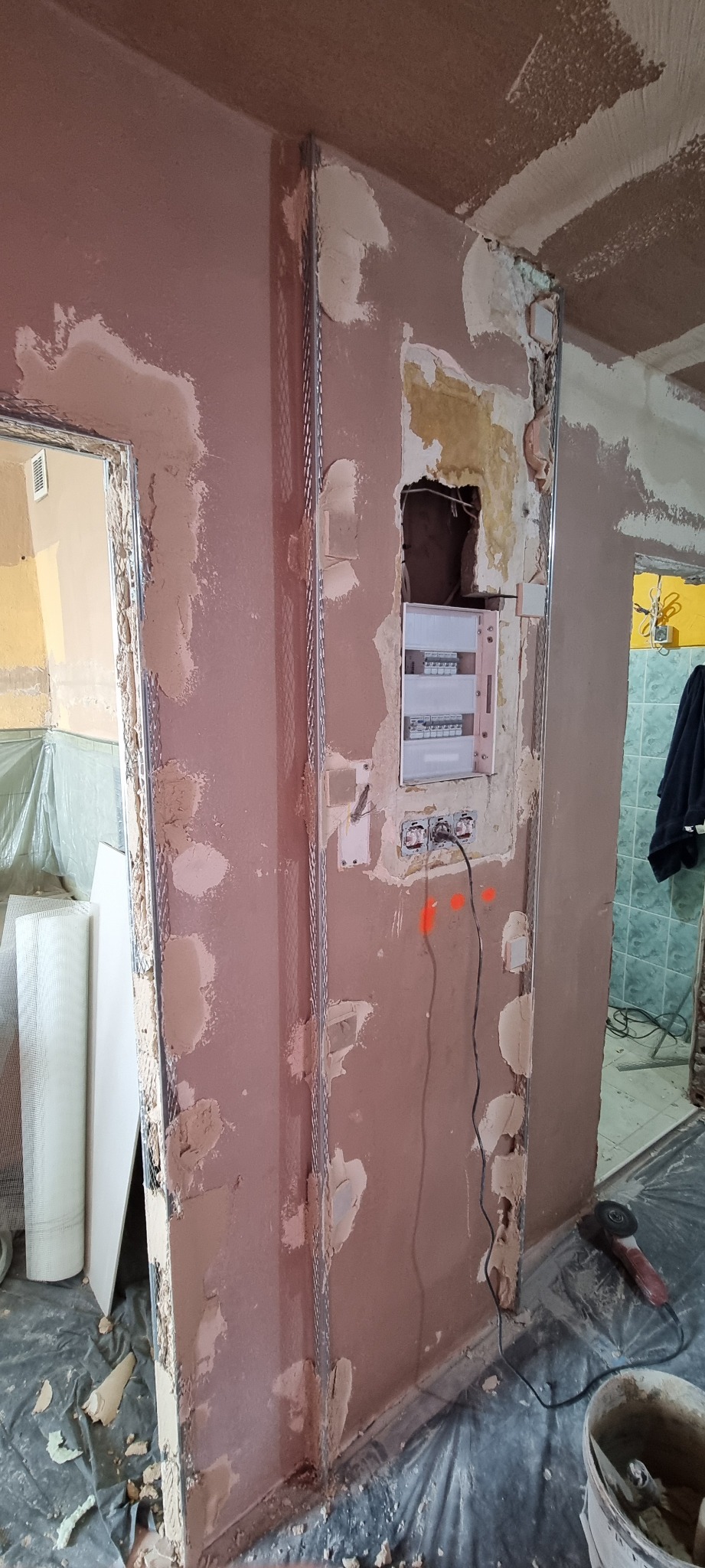 Ściana w trakcie przygotowania pod gładzie, z widocznymi metalowymi profilami, częściowo pokryta masą szpachlową, z otwartą skrzynką elektryczną i narzędziami.