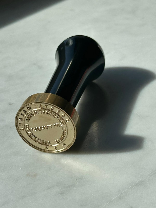 Złoty stempel z czarną rączką na marmurowym tle, rzucający wyraźny cień.