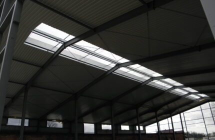Wnętrze hali stalowej z widoczną konstrukcją dachu, blachą trapezową i oknami dachowymi przepuszczającymi światło dzienne.