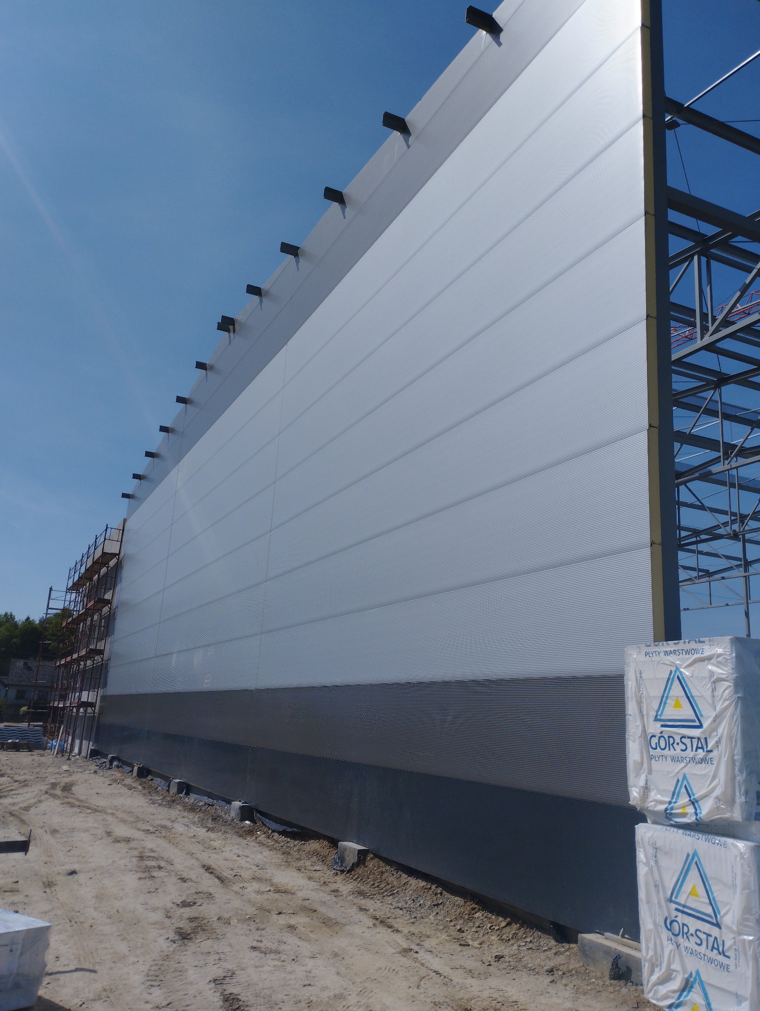 Montaż ściany hali z płyt warstwowych GOR-STAL, widoczne rusztowania i konstrukcja stalowa w tle.