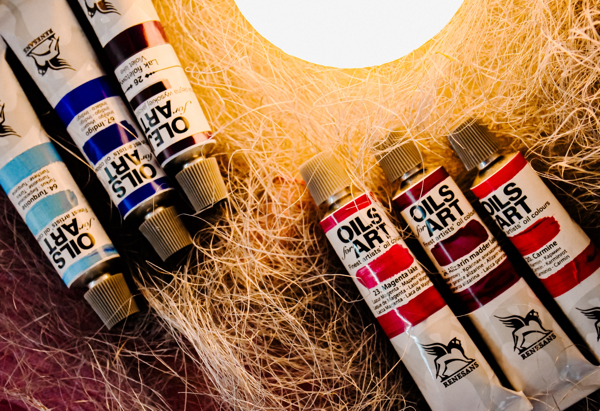 Kolorowe tubki farb olejnych marki Renesans ułożone na tle z włókien, oświetlone ciepłym światłem