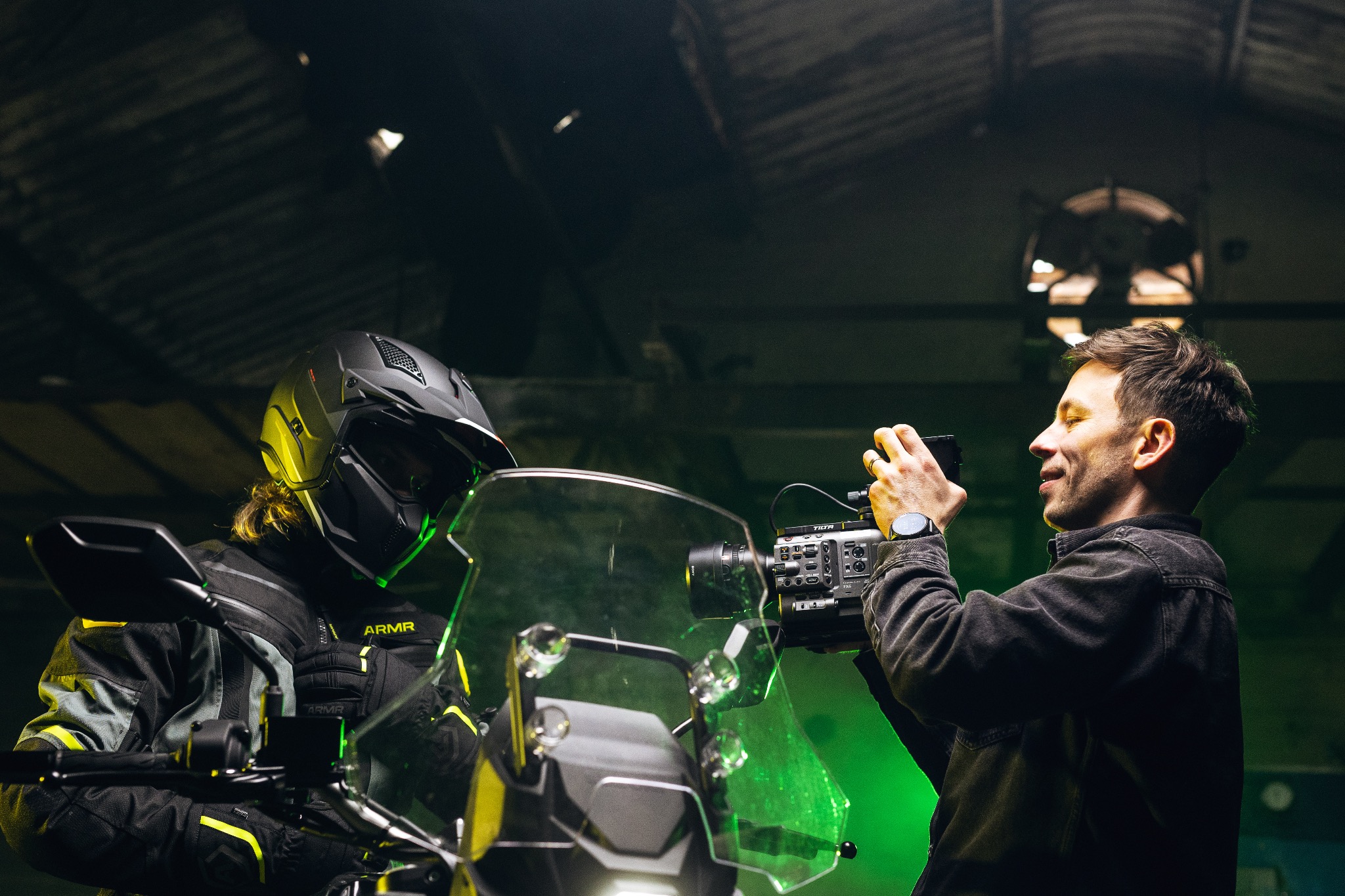 Operator filmuje motocyklistę w kasku i kurtce ARMR, używając kamery Sony FX6 z osprzętem TILTA w hali z surowym oświetleniem.