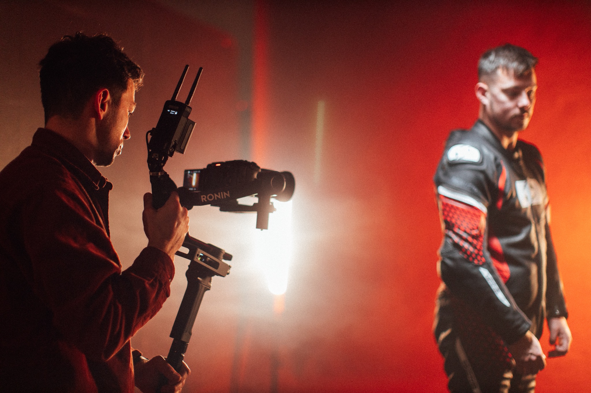 Operator kamery z gimbalem Ronin filmuje mężczyznę w skórzanym kombinezonie na czerwonym tle.