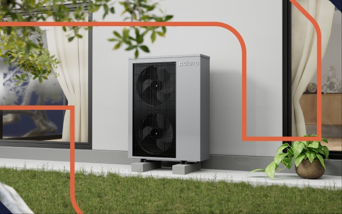 Szara, dwuwentylatorowa jednostka zewnętrzna z logo na białej ścianie domu, umieszczona na betonowych blokach, widoczna z trawnika, z oknami po bokach.