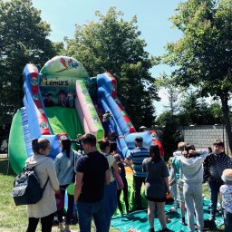 Watę Lizać - Dmuchana zjeżdżalnia z motywem dżungli i napisem 'Lemurs' otoczona grupą dzieci i dorosłych na trawiastym terenie w słoneczny dzień.