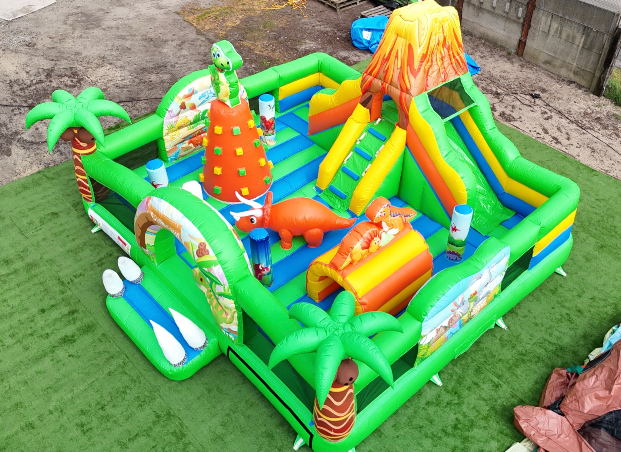 Kolorowy, dmuchany park rozrywki z motywem dinozaurów i wulkanu, widok z góry, rozłożony na sztucznej trawie w Pobiedziskach.