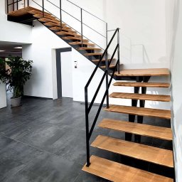 DomLoftu - Nowoczesne schody metalowe z drewnianymi stopniami, czarne poręcze, minimalistyczny design, widok z dołu, szare płytki podłogowe.
