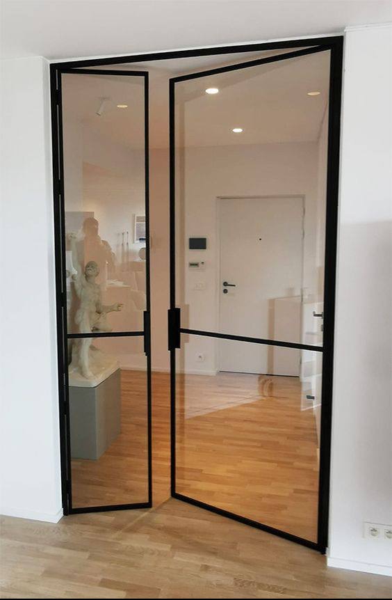 Rozwarte, dwuskrzydłowe drzwi szklane z czarną ramą, widok na wnętrze z parkietem, białą ścianą i rzeźbą klasyczną na cokole.