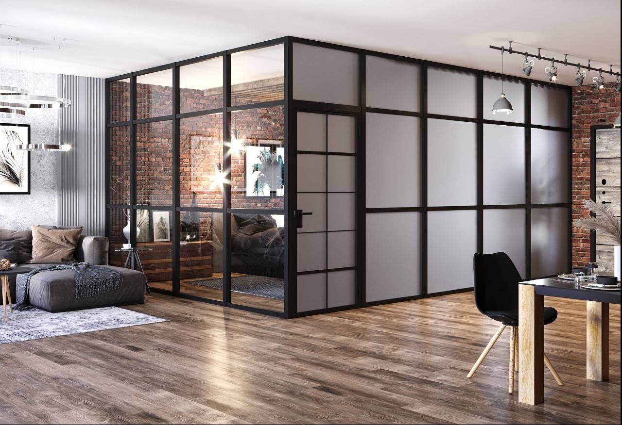 Loftowe wnętrze z przeszkleniami w czarnych ramach, oddzielającymi salon od sypialni z ceglaną ścianą i minimalistycznym wystrojem.