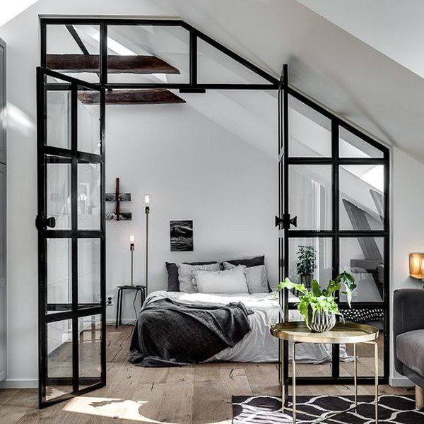 Nowoczesna sypialnia na poddaszu z przeszklonymi drzwiami w czarnej ramie, otwartymi na oścież, widoczne drewniane belki stropowe i minimalistyczny wystrój.