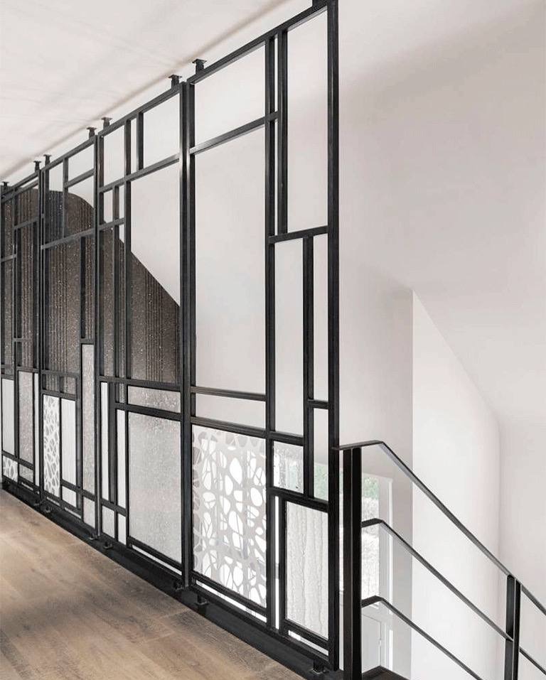 Nowoczesna balustrada schodowa z czarną metalową ramą i wypełnieniami z różnych rodzajów szkła, w tym szkła ornamentowego i przezroczystego, zamocowana do sufitu, widok z dołu schodów.