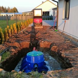K.P. Digger - Niebieska przydomowa oczyszczalnia ścieków w wykopie, z widoczną mini koparką Kubota w tle, na tle domu jednorodzinnego i tuj.