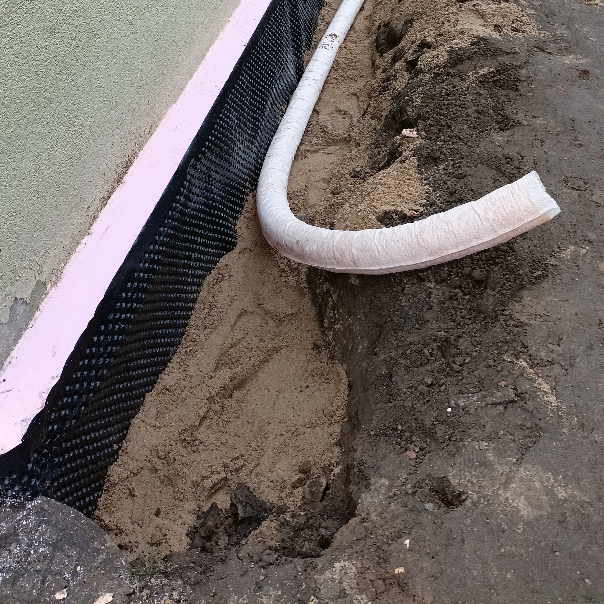 Fundament zabezpieczony izolacją pionową i drenażem w wykopie. Izolacja z folii kubełkowej, różowy styropian. Rura drenażowa w geowłókninie. Piasek zasypowy.