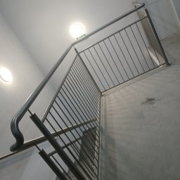 PIOTR TREPCZYK USŁUGI SPAWALNICZE - Wewnętrzne schody z metalową balustradą o prostych szczeblach, widok z dołu, oświetlenie sufitowe
