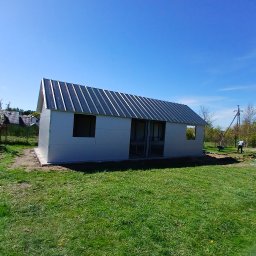 PIOTR TREPCZYK USŁUGI SPAWALNICZE - Nowy garaż blaszany z metalowym dachem, częściowo otwarty, na trawniku w słoneczny dzień. Widoczny fundament i otwory okienne.