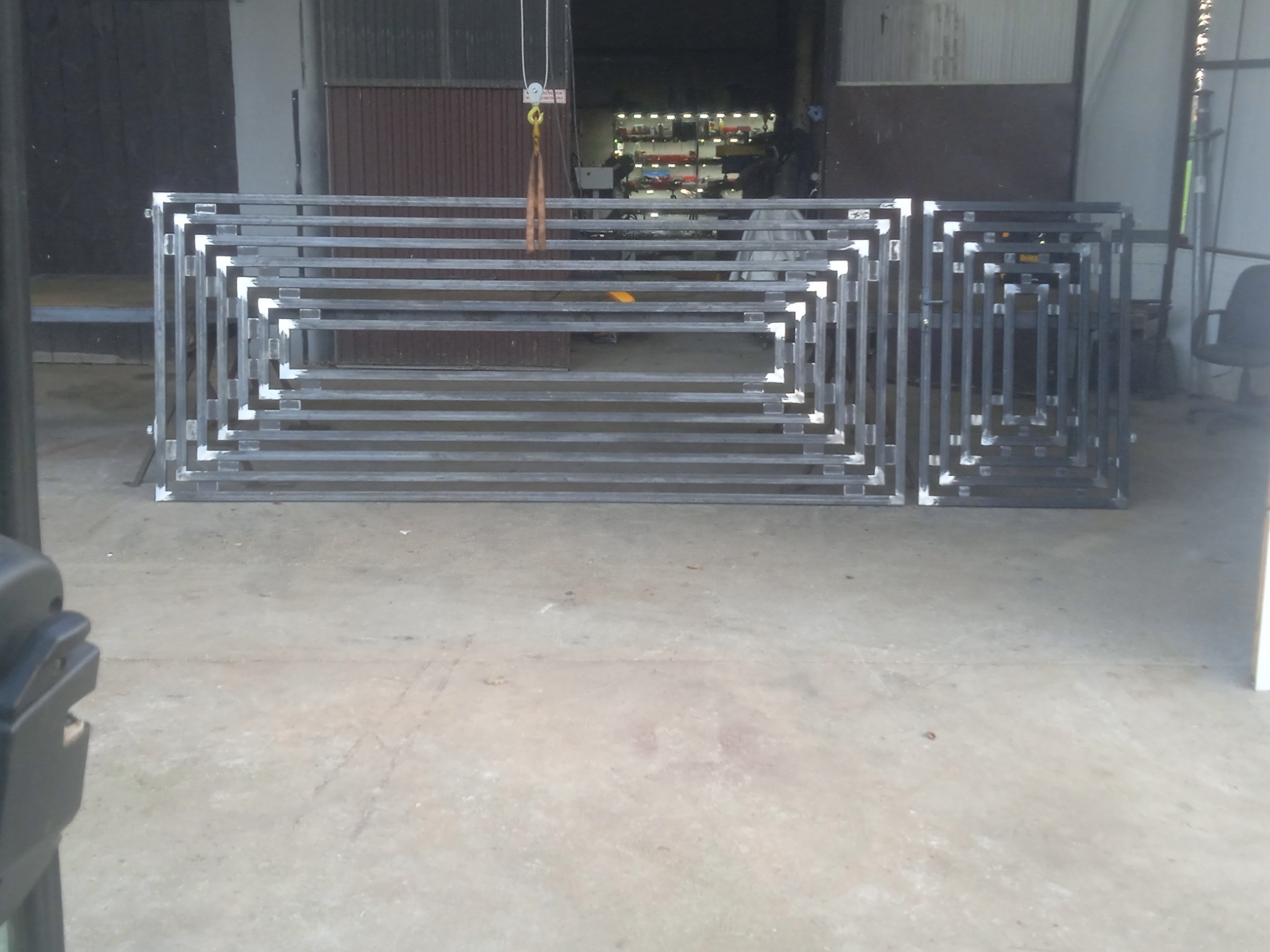 Metalowa konstrukcja bramy wjazdowej z kwadratowym wzorem, w trakcie produkcji w warsztacie, widoczne spawane łączenia, surowy beton na podłodze.