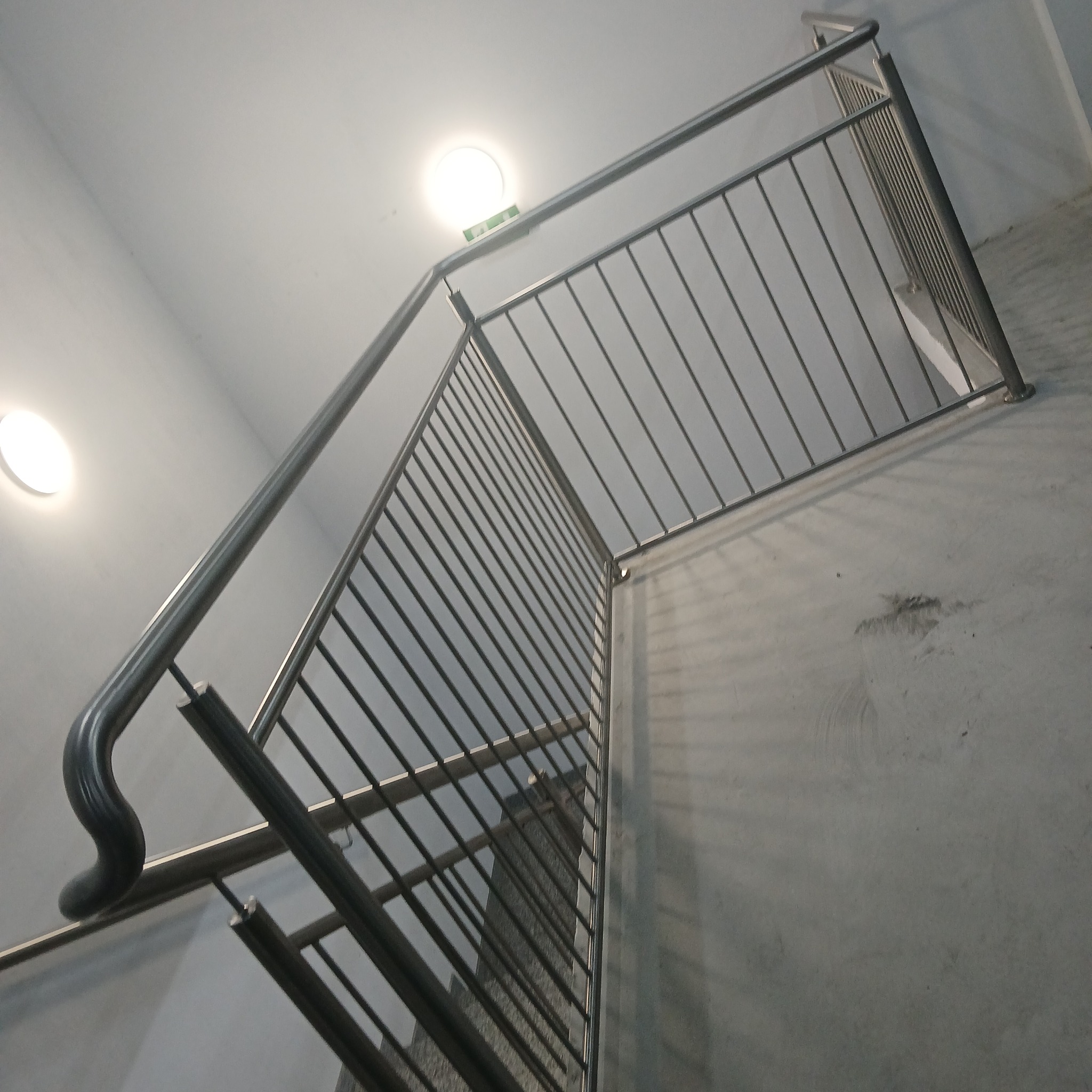 Wewnętrzne schody z metalową balustradą o prostych szczeblach, widok z dołu, oświetlenie sufitowe