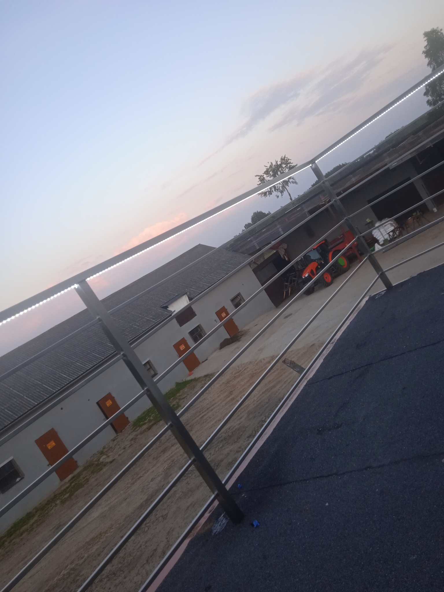 Metalowa konstrukcja z oświetleniem LED na zewnątrz budynku gospodarczego, widoczny traktor. Ujęcie z dołu, wieczorne światło.