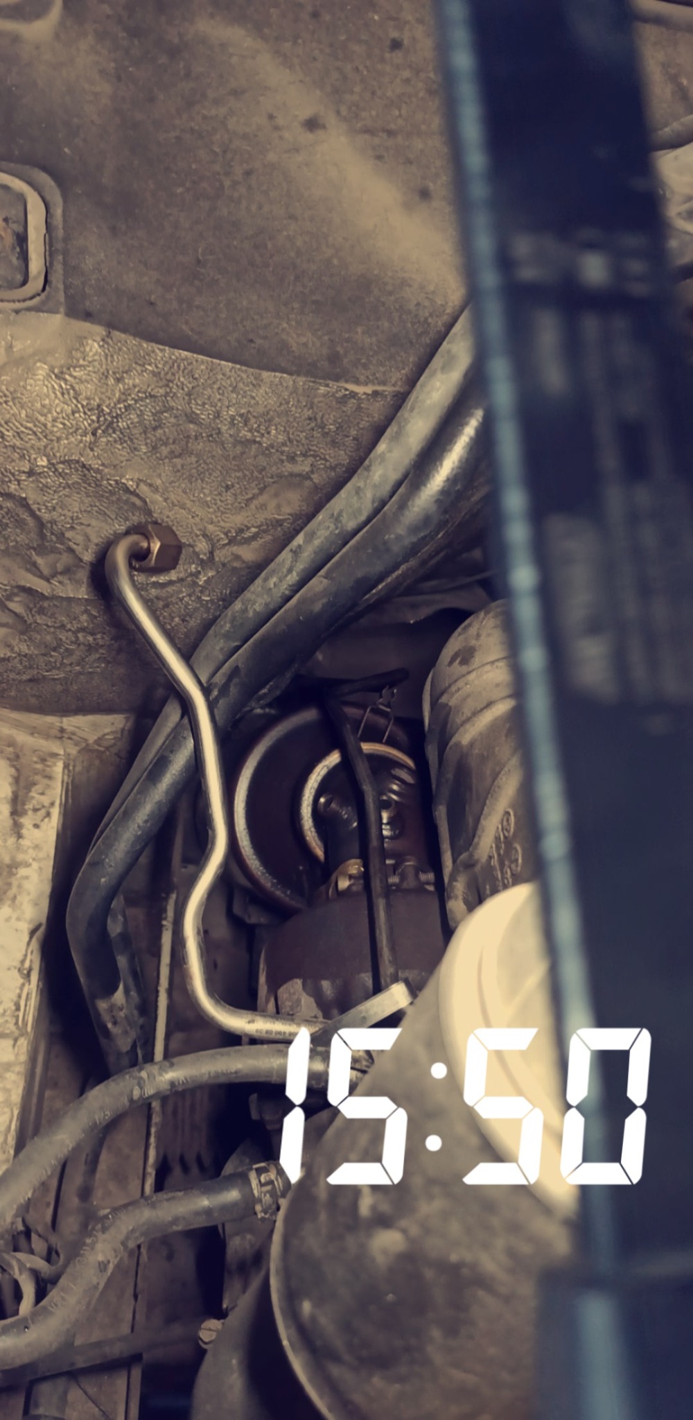 Widok z bliska na silnik samochodowy z widocznymi przewodami, filtrem i paskiem klinowym, sfotografowany z nietypowej perspektywy.