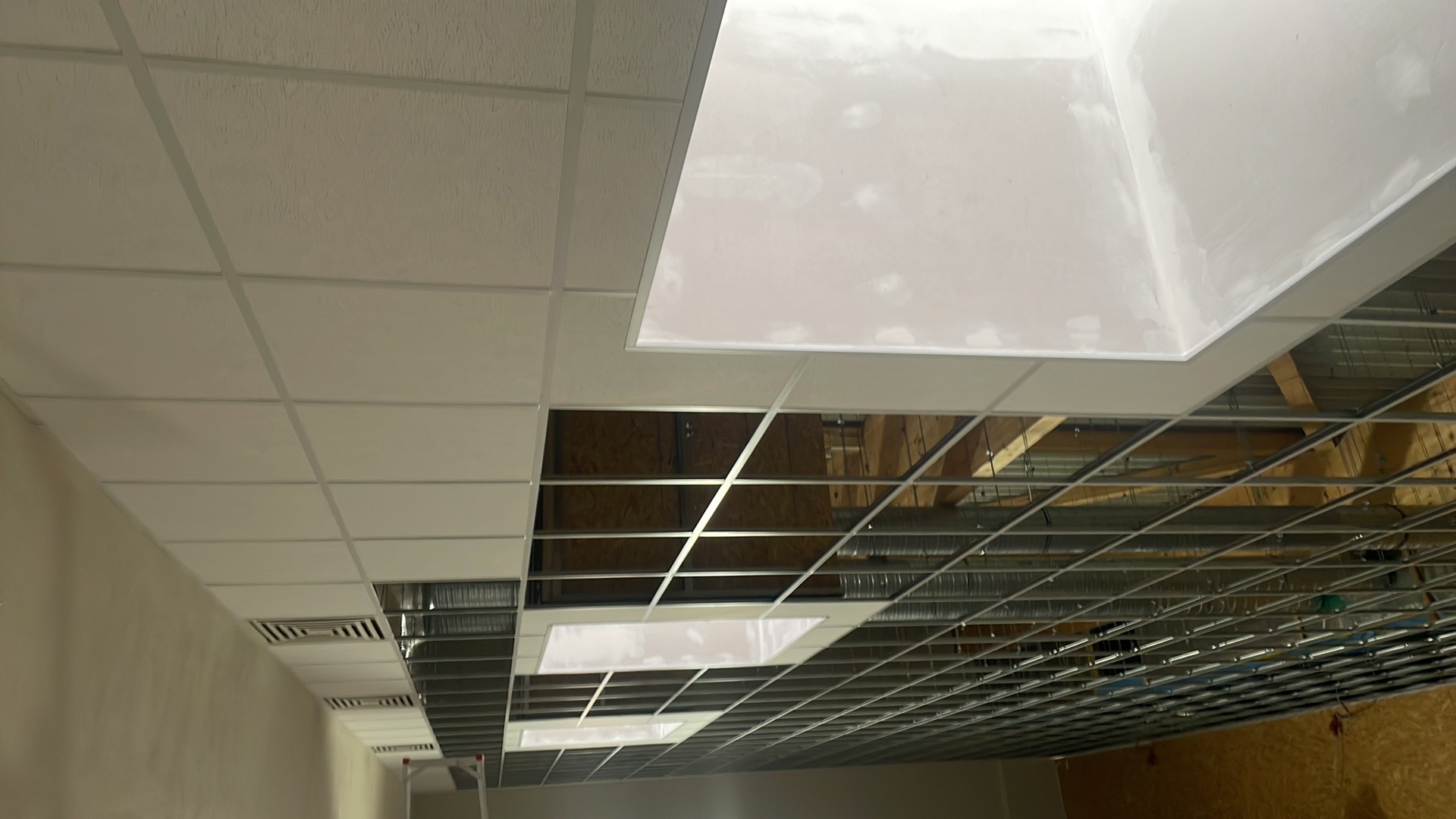 Kasetonowy sufit podwieszany w trakcie montażu, widoczne elementy konstrukcyjne i częściowo zamontowane płyty. Ujęcie z dołu, perspektywa wnętrza w trakcie prac.
