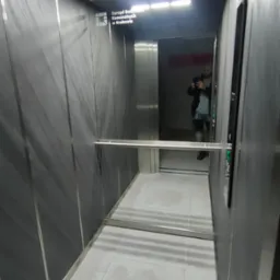 Wnętrze nowoczesnej kabiny z lustrem, wykończonej w odcieniach szarości, z widocznym panelem sterowania i oświetleniem sufitowym.