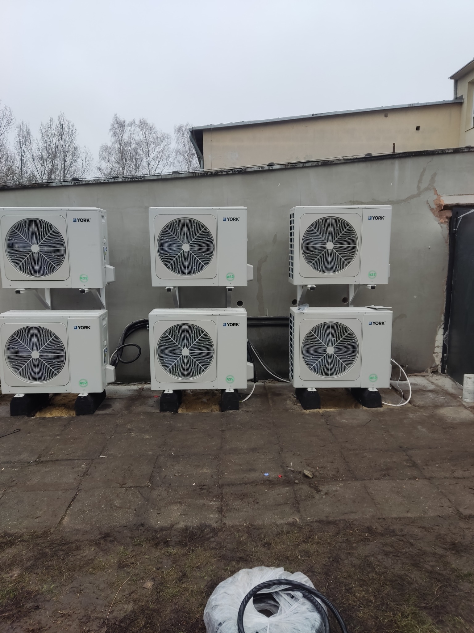 Sześć jednostek zewnętrznych klimatyzacji York, zamontowanych na szarym murze zewnętrznym budynku. Widoczne przewody i elementy montażowe.