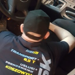 Błysk Śrem - Mężczyzna w czarnej koszulce z napisem 'TRANSPORT 8.5 T' siedzi za kierownicą samochodu marki Audi, widoczna kierownica, deska rozdzielcza i dźwignia zmiany biegów.