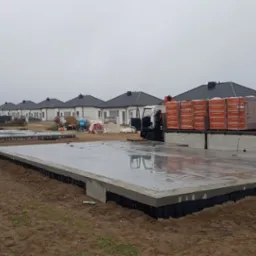 Przygotowane fundamenty pod budowę osiedla domów jednorodzinnych; na jednym z fundamentów zaparkowana ciężarówka z materiałami budowlanymi - cegłami Termoton.