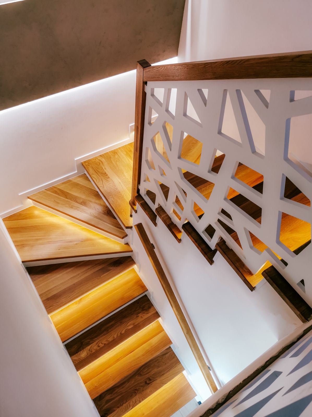 Nowoczesne schody z podświetlanymi stopniami i ażurową, białą balustradą z drewnianym wykończeniem, widok z góry.