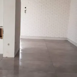 Ułożona szara podłoga z płytek w pomieszczeniu z białą cegłą na ścianie, widoczne niedokończone prace przy kolumnie i instalacji elektrycznej.