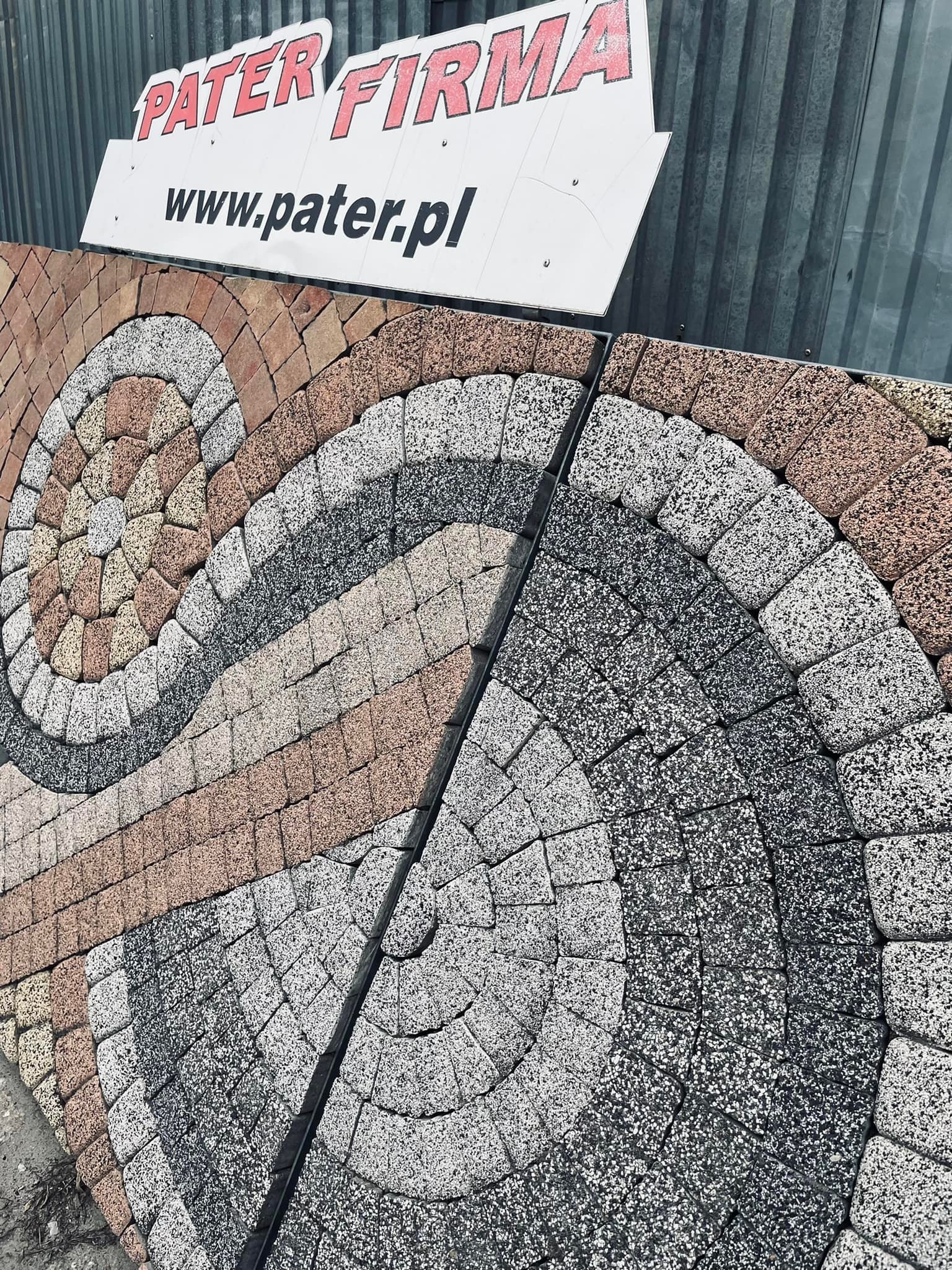 Ekspozycja wzorów kostki brukowej ułożonych w okrągłe motywy, z widocznym szyldem firmy 'PATER FIRMA' i adresem strony internetowej.