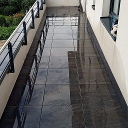 Damian Dawid - Długi balkon z ciemnymi, błyszczącymi płytkami, odbijającymi niebo, z czarną balustradą i piłką do nogi wystającą z okna.